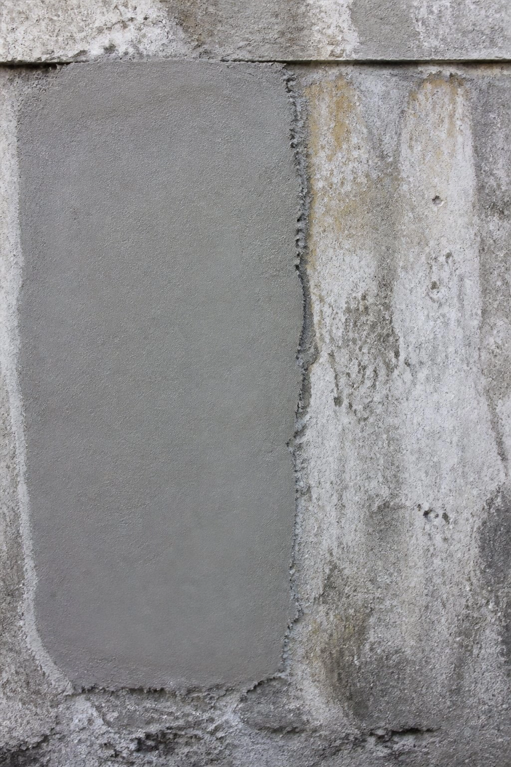 New concrete patch beside weathered water-stained wall surface